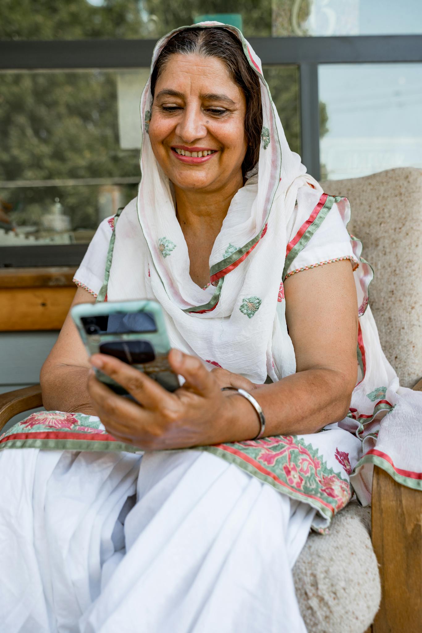 A joyful elderly woman in traditional attire using a smartphone outdoors.