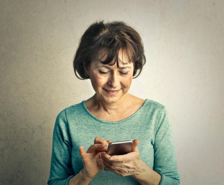 A senior woman smiling as she interacts with her smartphone indoors, expressing happiness and technology use.