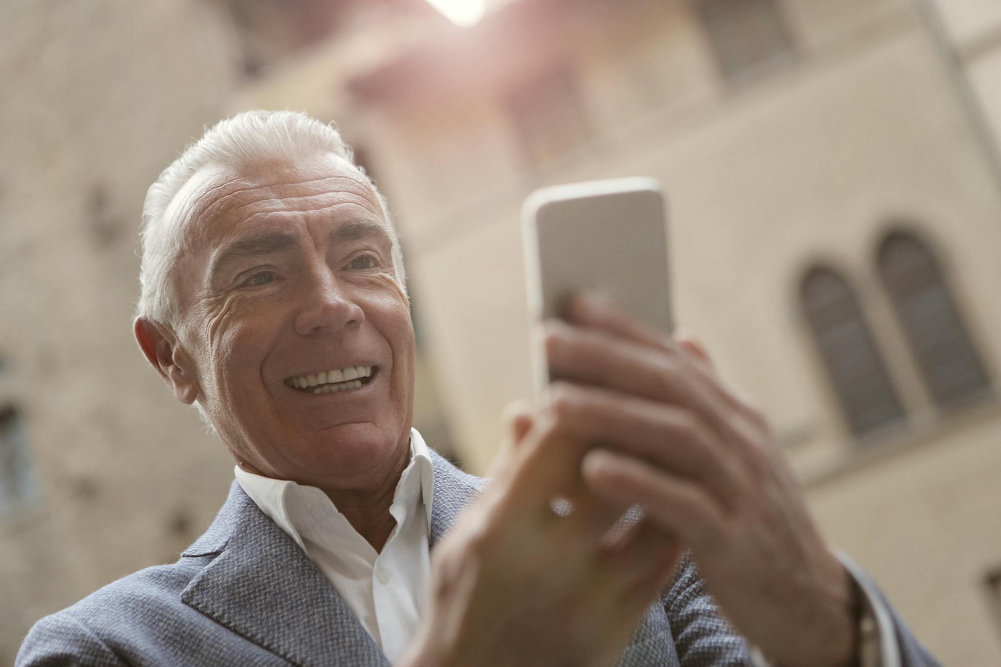 Elderly man smiling while video calling on a free government phone outdoors.