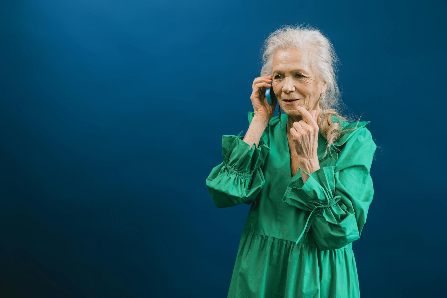 Senior woman in green dress talking on a mobile phone against a blue background.