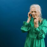 Senior woman in green dress talking on a mobile phone against a blue background.